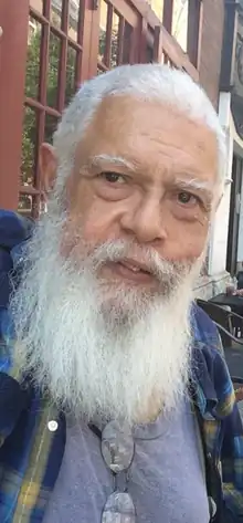Photographie couleur en gros plan de Samuel R. Delany, représentant un homme barbu et moustachu avec des cheveux blancs et des yeux sombres. La photo date de 2018 (13 ans après le décès d'Octavia Butler).