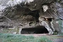 Vue de l’entrée d’une grotte, s’ouvrant comme une bouche dans une falaise de calcaire gris clair.