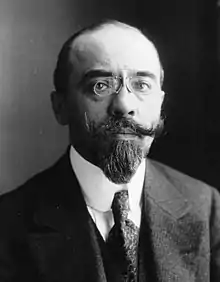 Photographie d'un homme blanc d'une quarantaine d'années, le front dégarni, des lorgnons sur le nez, portant des moustaches et une barbiche