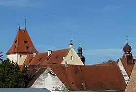  Photographie en couleurs montrant plusieurs bâtiments de couleur rosâtre coiffés de toits rouges sous un ciel bleu.