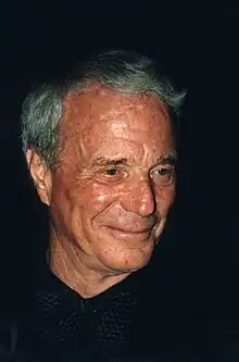 Gros plan sur le visage d'un homme âgé, portant une chemise et un nœud papillon noirs.