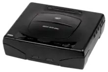 Photo d'une Saturn noir ; elle dispose d'un capot pouvant accueillir un CD et deux prises sur le devant pour brancher deux manettes