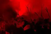Spectacle son et lumière de nuit/ Dans une lumière rouge évoquant le feu, des paysans hommes et femmes revêtus de costumes bretons traditionnels brandissent des fourches sommaires en bois