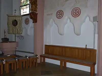 Photographie d'un banc de bois placé devant une triple niche creusée dans le mur d'une église.