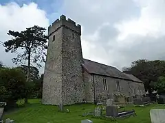 Photo d'un bâtiment allongé aux murs de pierre grise, flanqué d'une grande tour carrée au premier plan à gauche