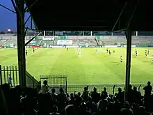 Stade de football avec plusieurs joueurs dedans, sous un ciel nocturne.