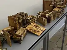 Une vingtaine de volumes de bois, semblables à des livres ; deux volumes ouverts contenant des rameaux feuillus