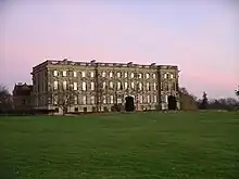 Au milieu d'une pelouse, façade d'un vaste bâtiment de trois étages sur rez-de-chaussée surélevé. 15 fenêtres par étage, un toit en terrasse bordée de colonnettes.
