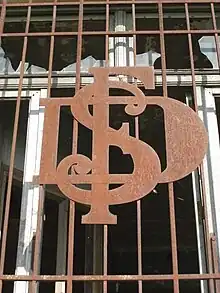 Sigle S.D.F. (Sucrerie et Distillerie de Francières) en métal forgé sur des barreaux de fenêtres de bureau. Les lettres S, D et F sont entrelacées.