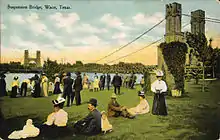 Carte postale dépeignant en couleur des habitants devant le pont suspendu de Waco.