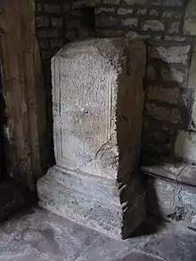 Photo d'un bloc de pierre en forme de parallépipède, ébréché au sommet, portant sur une face une inscription en grandes capitales profondément gravées