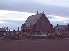 Église de grès rose et de style néogothique bâtie au milieu d'un cimetière.
