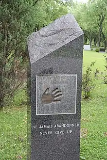 Photographie couleur de la tombe de Maurice Richard. Il y a l'empreinte d'une main ainsi que la mention en français Ne jamais abandonner puis en-dessous en anglais Never give up.