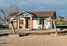 Photo de la mairie d'Espaon éclairé par le soleil couchant : petit bâtiment de plein pied, la porte est protégée par un porche. Deux fenêtres sont situées de part et d'autres de la porte, cerclées de briques. Celle a droite à des volets bleus. Le toit du bâtiment est en tuiles.