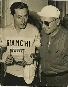 Photo en noir et blanc montrant deux hommes, celui de gauche est en tenue de cycliste, celui de droite plus âgé porte une casquette et des lunettes de soleil.