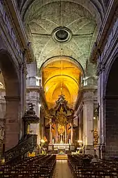 Photographie du vaisseau central de l’église, prise depuis l’entrée. Le chœur est brillamment éclairé.
