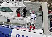 Armel Le Cléac'h, debout sur son bateau, saluant la foule