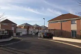 Vue d'une résidence pavillonnaire moderne ; bâtiments de même modèle alternant pierre et brique.