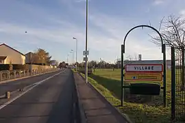 Panneau indicateur à l'entrée d'une commune ; parc de la salle des fêtes à droite ; zone résidentielle à gauche.