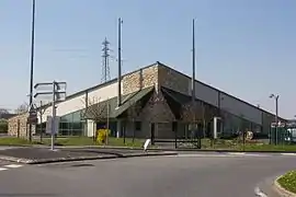 Vue d'un bâtiment moderne partiellement en meulière et à toiture à facettes ; deux mâts près des entrées.