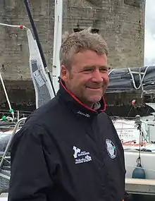 En buste, de trois quarts, dans un port, au pied d'une tour moyenâgeuse.