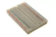 Image d'une breadboard : une plaque rectangulaire bordée de trous.