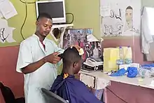 Photographie d'une homme manipulant un rasoir sur la tête d'une autre personne.