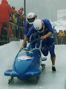 Photographie de deux personnes autour d'un traineau en métal.