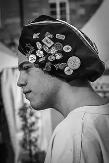 Photographie en noir et blanc d'un homme de profil avec un chapeau mou recouvert de badges.