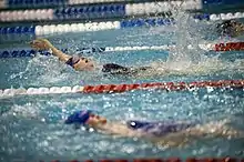 photographie : un bassin, une jeune femme nage sur le dos, dans le fond d’autres nageuse