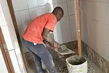 Photographie d'un homme en train de déposer du ciment sur un carreau.