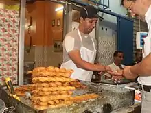 Photographie d'un homme derrière un étal recouvert de pâtisseries longues et torsadées.